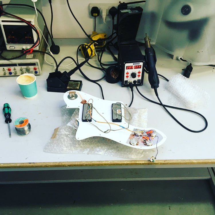 The pickguard of the tele deluxe sites on an electronics workbench, rear-side up, showing the pickup wiring being worked on.