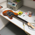 An orange guitar sites on the workbench looking close to complete.