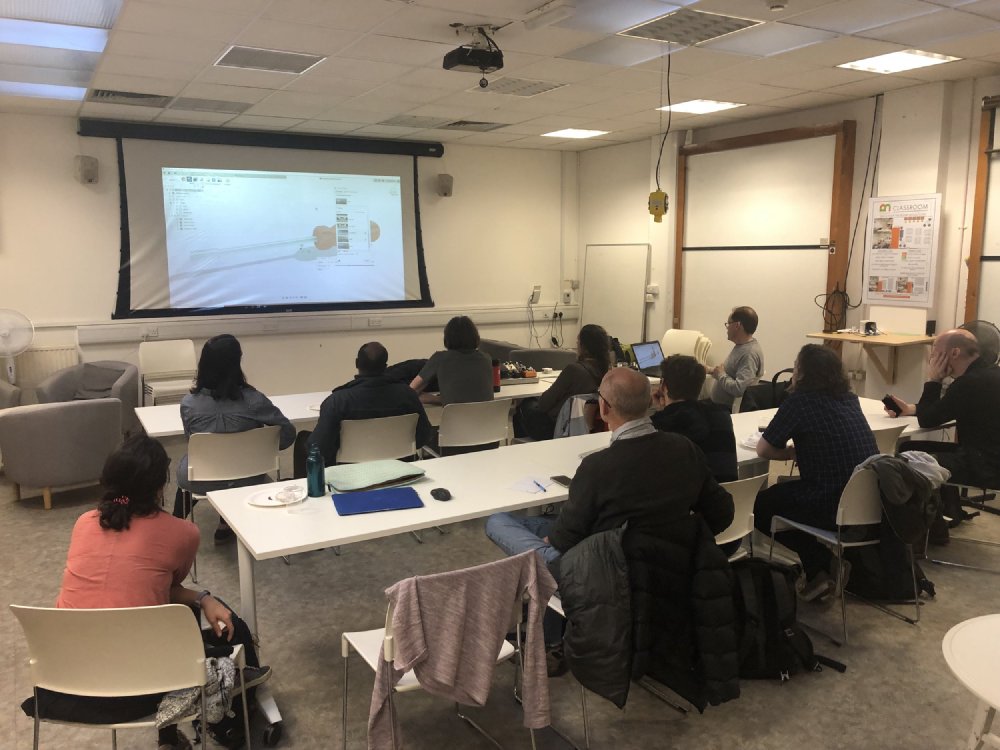 A photo of a classroom of ten people looking at a projection of someone's Fusion 260 project.