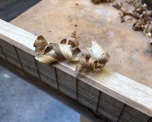 The side profile of a guitar neck being built, with some shavings on it from being planed. The shavings are two coloured, as both the dark wood of the fretboard and the light wood of the neck have been shaved.