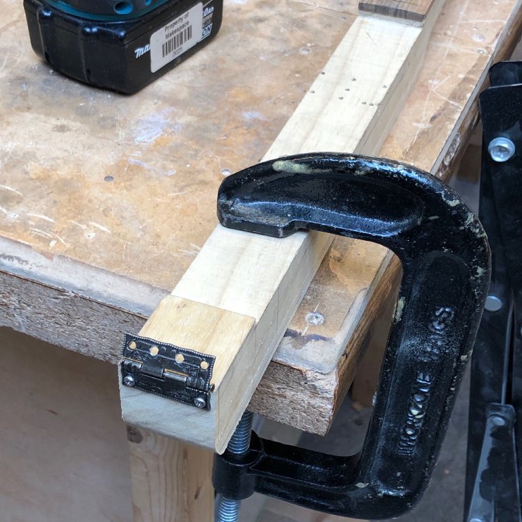 The tail end of the neck of the cigar box, which runs all lenght of the instrument, sits clamped to the workbench, and you can see a small ornate hinge has been attached.