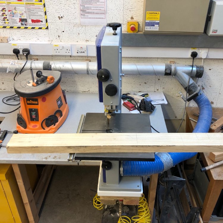 A blank of wood sits on the table of a bandsaw ready to be chopped.