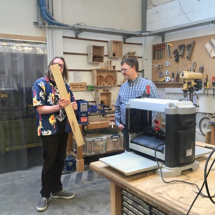 Myself, wearing a hawaiian shirt indicating it must be Friday, and Adrian are testing out the new thicknesser, which sits on the workbench next to us. I am holding a plank of wood ready to feed to the thicknesser.