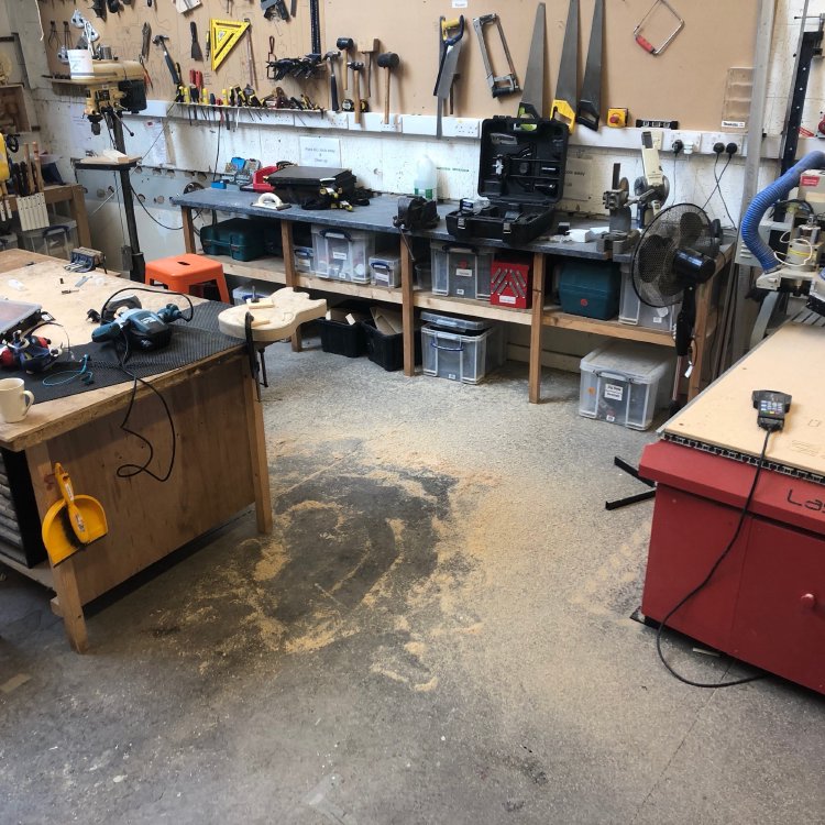 The same scene as the last photo, but taken a few steps back. The guitar body is now flush with the template, and the workshop is covered with a lot of wood dust, getting more concentrated as you go towards the guitar body.