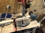 A roughly shaped guitar neck is on a pillar drill, with the holes for the tuning pegs being drilled.