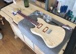 An in-progress pointy-offset style guitar build sits on the workbench surrounded by bags of parts. The neck, which maple with a purpleheart fretboard, is mostly completed but un-oiled, and the body is shaped and sanded, but is yet to have holes put in it for pickups and controls. On top of the body sit a bunch of parts placed to give an idea of how it'll look when finished.