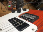 The 3D printed bridge mounted on the guitar with strings running over it. In the background you can see the floor and my pedal board, telling you that this is now being used!