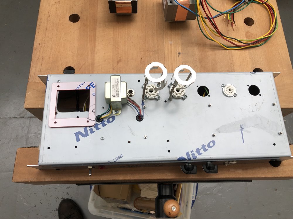 The chassis sits bottom side up, showing the second output transformer (the amp has two transformers), where the valves go, and then over the hole where the old transformer was sits the acrylic template I cut to give me a cutting guide for making a new larger hole.