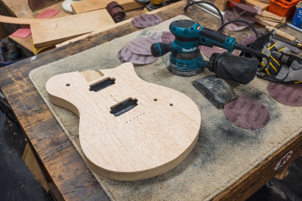 The body face up on the workbench, next to a random-orbital-sander, and a stack of sanding disks.