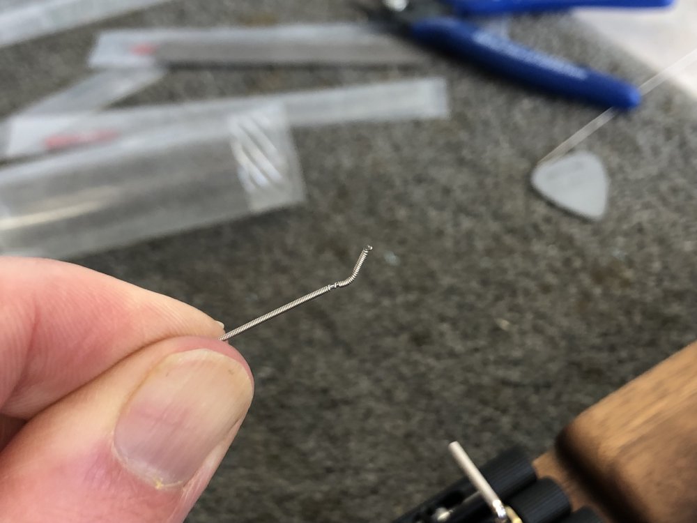 A close up of the end of a guitar string. You can see a V like pinch close to the end from where it's been clamped in the bridge tuners on Älgen, and on the string-side of that pinch you can see the outer winding of the string has started to unravel.