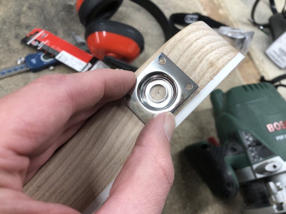 A close up of the side of the guitar body, over which I'm holding in place the square metal plate for mounting a jack onto the side. I'm holding it so that the place is centred on the wooden part of the side of the body, ignoring the white plastic binding around the top.