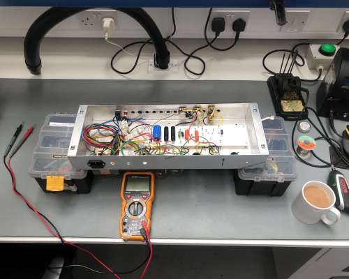 The open chassis of the valve amplifier sits on a workbench, next to which sits a multimeter and a fresh cup of tea.