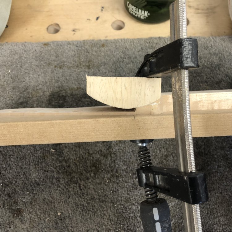 A close up of the headstock transition part of the neck, showing a rounded bit of wood (that was a test carve of a neck by another luthier in the workshop) clamped over the join as I try to glue the fretboard material back down where it had de-laminated.