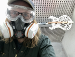 A selfie of me in the spray booth, wearing all my PPE (respirator, eye-protectors, goggles), and behind is the over-exposed 3D-printed body of a guitar ready for spraying with lacquer.