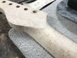 A close up of an in-progress neck carve, showing the transition between the headstock and the back of the neck. The neck is made from bird's eye maple.