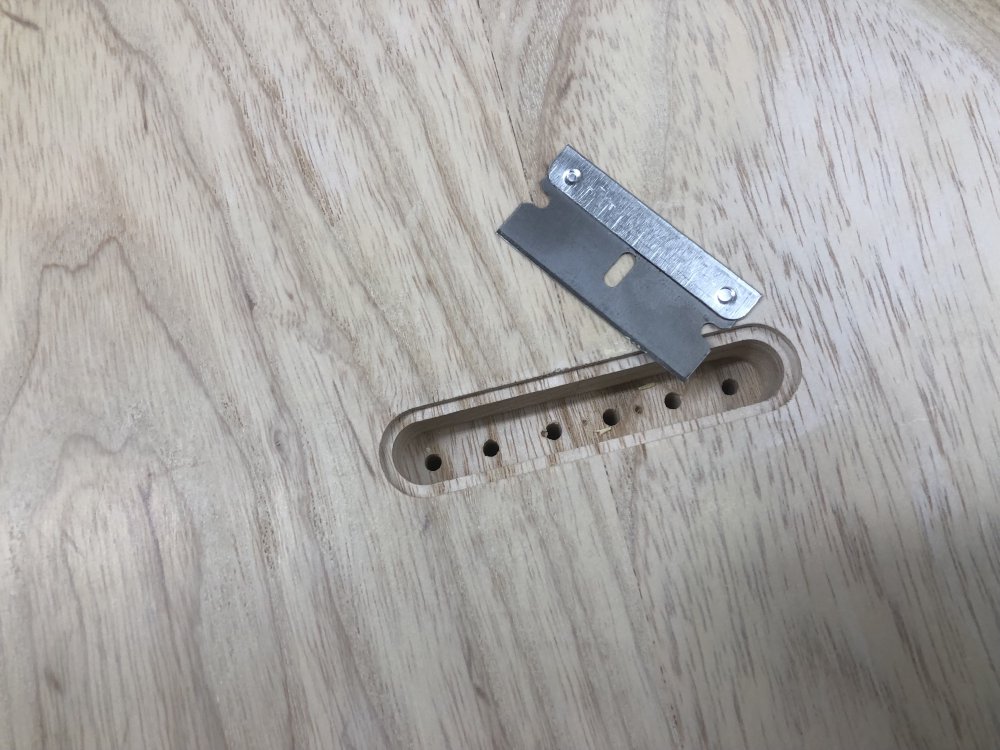 A close up on the rear of the guitar body where the ferrule block will be inserted, which has a well defined stepped edge. Next to it sits a razor blade.