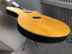 A shot of a guitar body still in a clamp in a spray-booth, showing a yellow stained birds-eye maple front, and then about 5mm of natural wood colour as you go down the side, and the rest of the side is black paint.