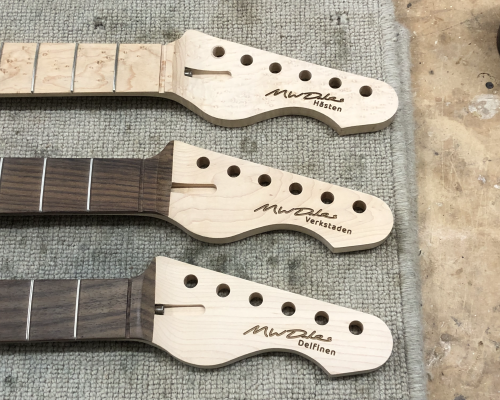 A close-up of three headstocks, with my signature and guitar's name laser etched into the headstock.