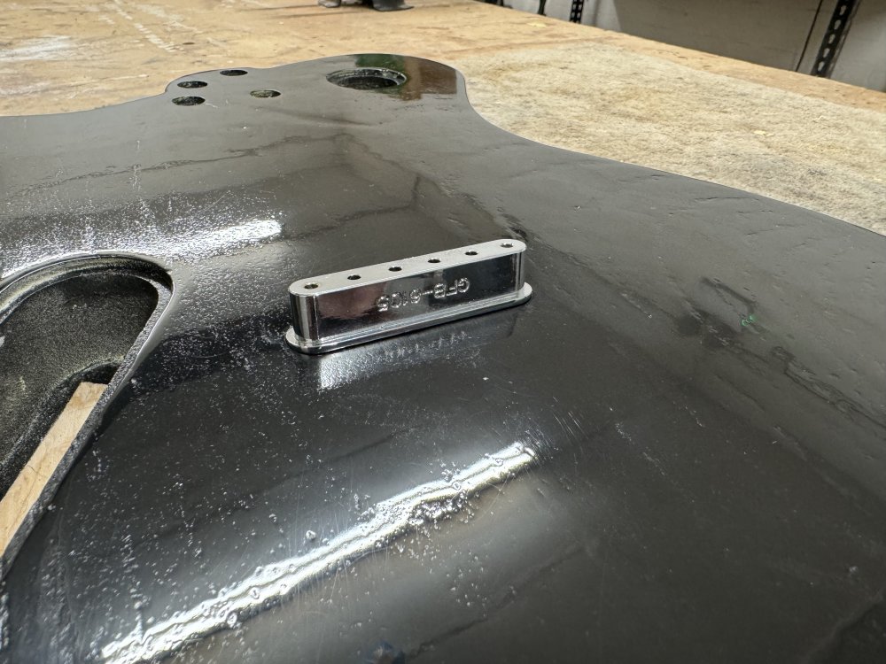 A close up on the back of the guitar, showing the cavities for the electronics. In the middle of the back is a chrome metal block with 6 holes in it. This is sitting over the hole it should sit in, as it no longer fits due to paint build up.