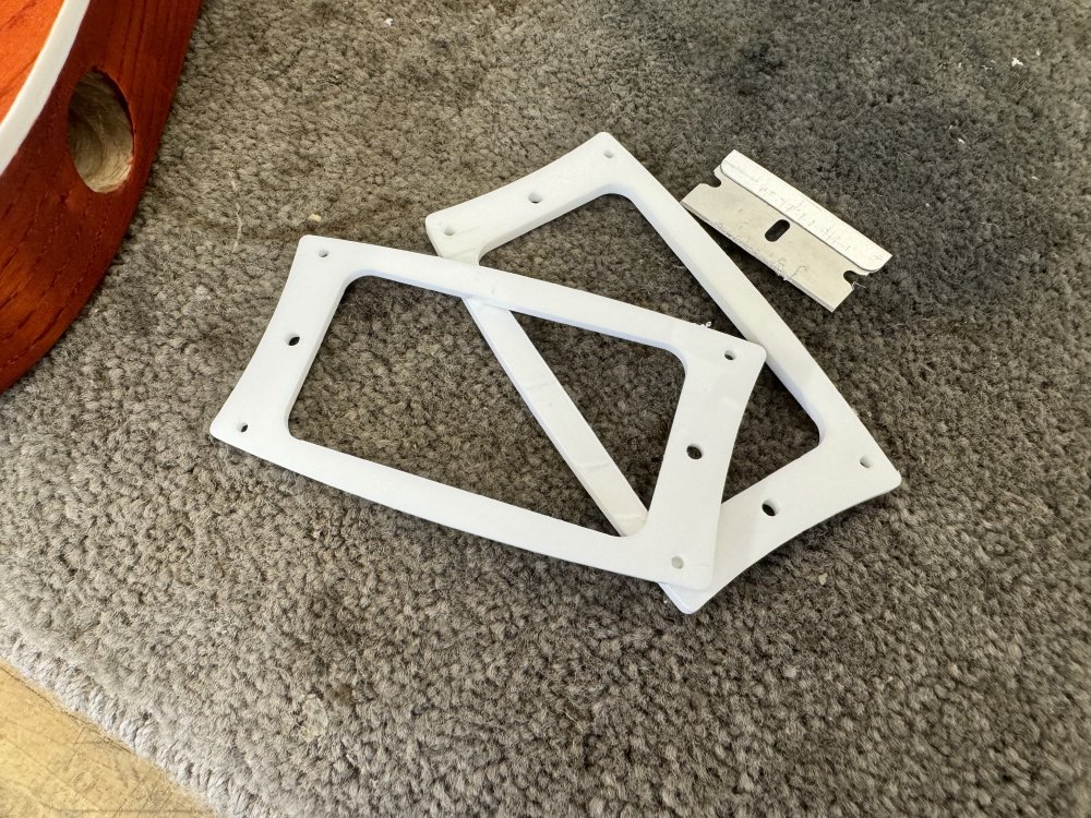 Two white-acrylic pickup mounts sit on a workbench next to a razor blade.