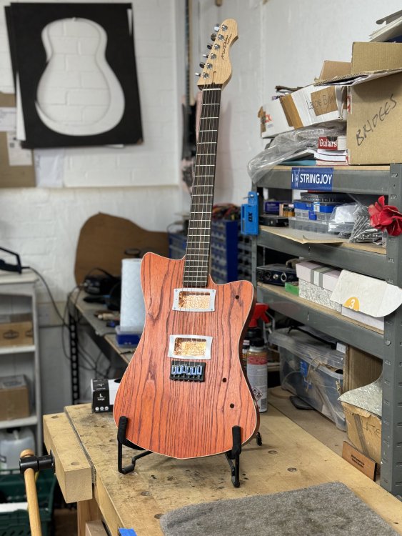 The guitar mostly assembled guitar again, this time stood in a guitar stand on the workbench.