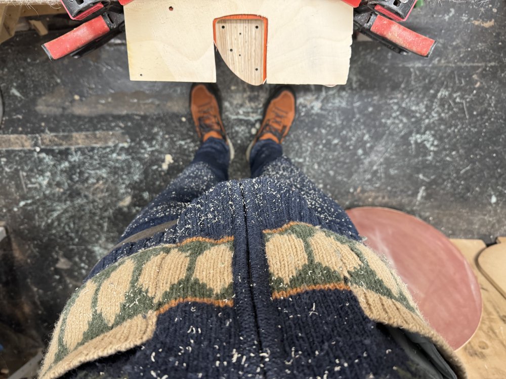 A first-person view photo looking down at my body next to the guitar body being worked on. My torso is covered with wood-dust.