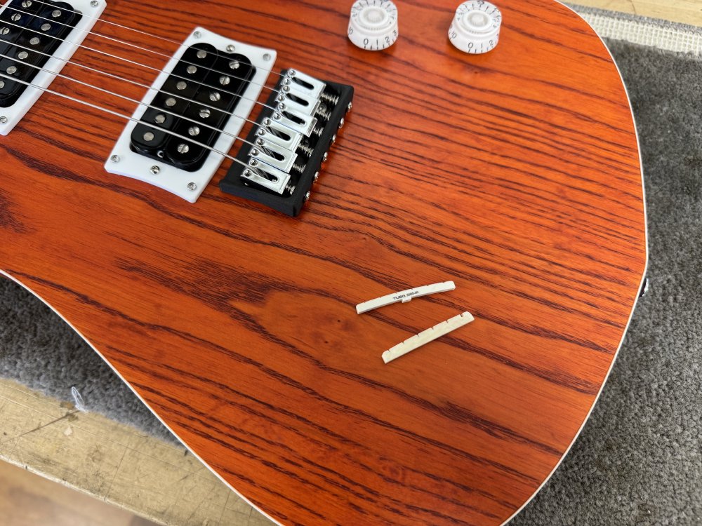 A photo of two guitar nuts: one is made of bone, looking slightly cream coloured, and the other is a vibrant white being made of a synthetic material.