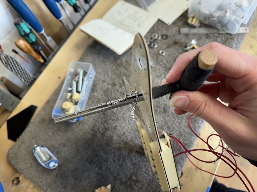 A photo of me holding a pickguard, which has a T shaped tool (a woodworking hole reamer) poking through it.