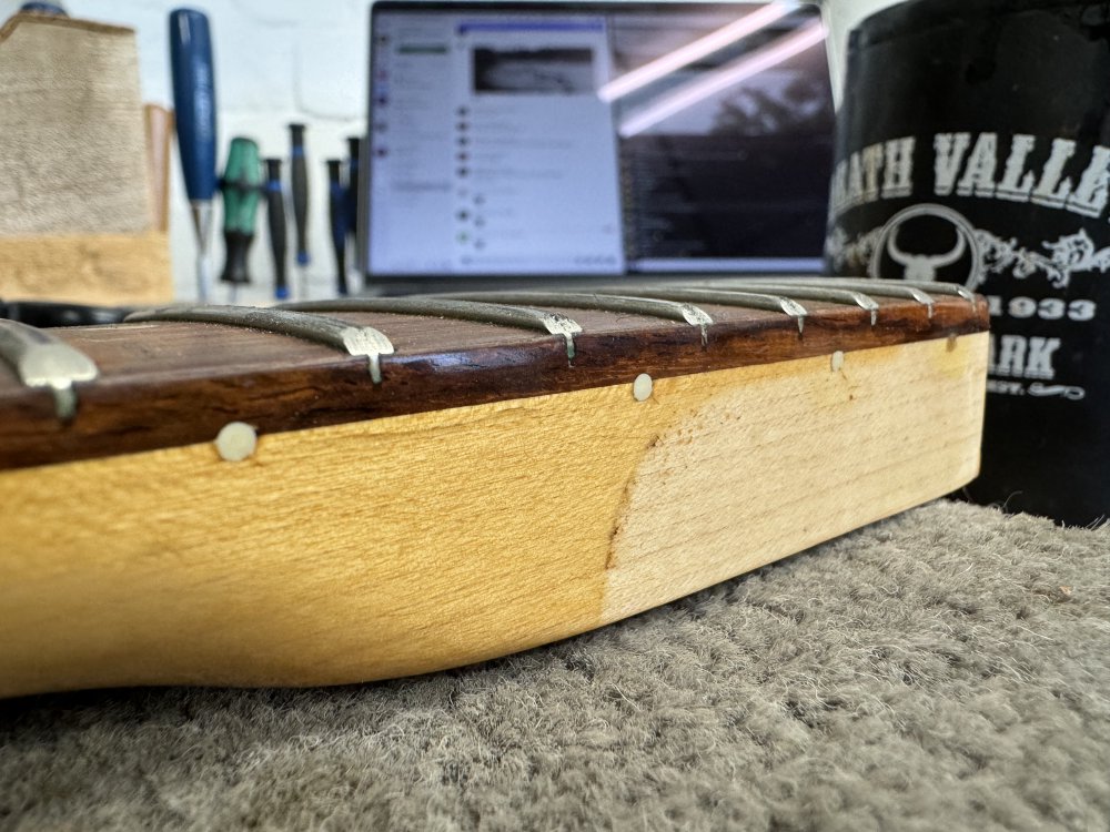 A close-up photo of the neck from the strat-close, showing the join between the fretboard and the main neck, down at the heel end. You can see the last four dot inlays go from being on the fretboard join line to underneath it. But you can also see from the faded lacquer that the last dot that is the worse wouldn't be visible when the neck is installed in the body.