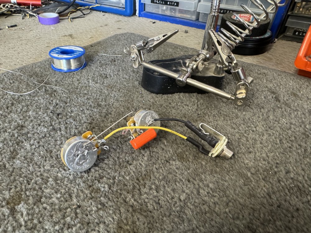 A photo of the two potentiometers, a large orange-drop capacitor, and the input jack wired  and soldered together on a workbench outside of the guitar itself. My soldering isn't the best, but is better than it used to be.