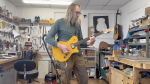 A photo of me stood in the workshop playing a solid-bodied electric guitar that has a bright yellow wood stained body, a rosewood fretboard and a maple neck. I appear to be playing an A barre chord.