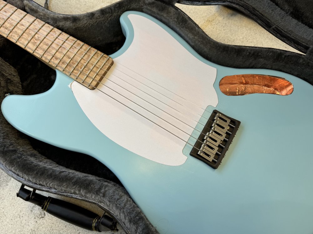 A photo of the paper-cut pick-guard placed onto the guitar we saw earlier in the location the final pick-guard will go. Where there is space for the bridge in the pick-guard it can be seen there is more space on the top edge than on the two side edges, making it appear sloppy.