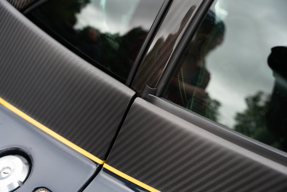 A close up photo of a where a car door joins the rest of the car at the point the window also joins the door body. The door and body are made from carbon-fibre, indicating it's an expensive car. Around the window you can see the normal rubber seals to prevent water getting in, but there's also a bit of a rubber seal coming up from the main door body that looks out of place in an otherwise well appointed car.