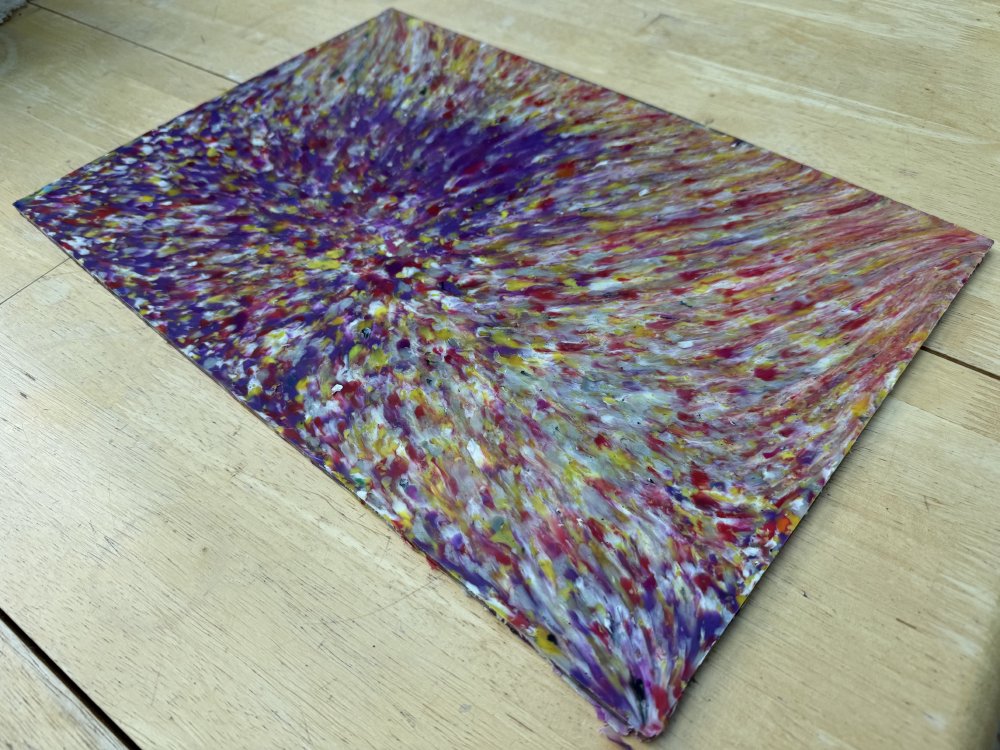 A photo of a sheet of plastic about A4 or slightly bigger in size. It's mostly purple but also full of whites and yellows, all flowing to an off-centre point, and it looks like an oil painting.