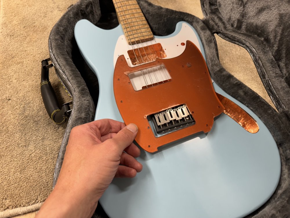 A photo of me holding the copper-coloured pick-guard over the blue painted guitar body to show how the colours don't really match.