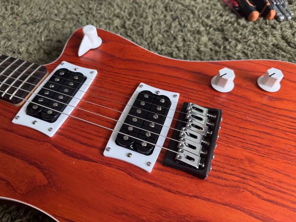 A close-up photo of the body of an orange guitar that has uncovered humbucker pickups mounted on it. Each pickup can be seen to be constructed from two black bobbins with six metal pole pieces in each bobbin, one pole piece under each string.