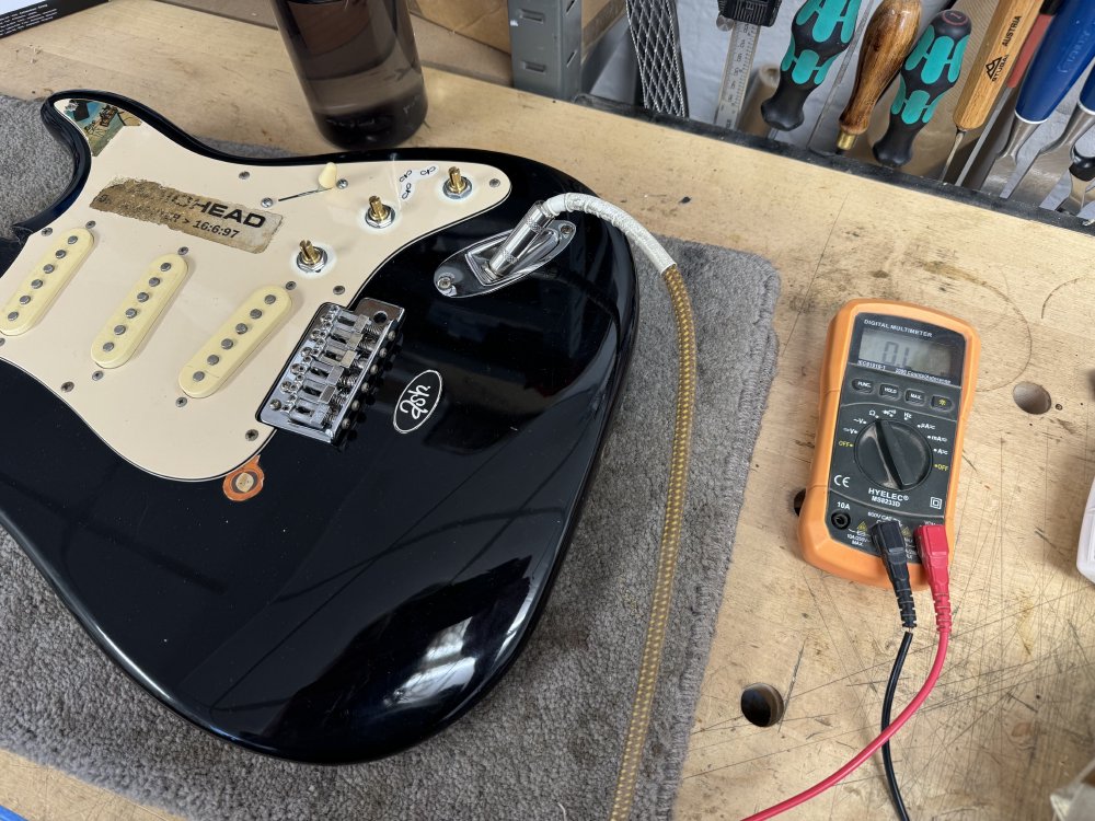 A photo of a guitar body of the black electric guitar with a multimeter connected to the jack socket.