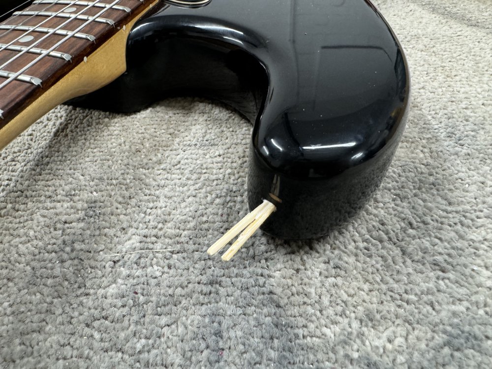 A photo of the upper horn of an electric guitar body, and where the strap-button should be is a hole with three tooth-picks sticking out of it.