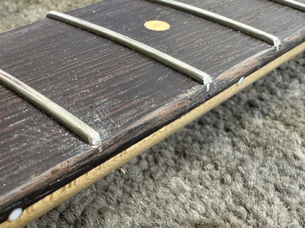 A macro close-up shot of two frets. One has been rounded into a hemisphere and is all scratched up from being recently filed. The other is clearly bevelled and has a distinct set of facets at the end, creating edges that the hand will feel.