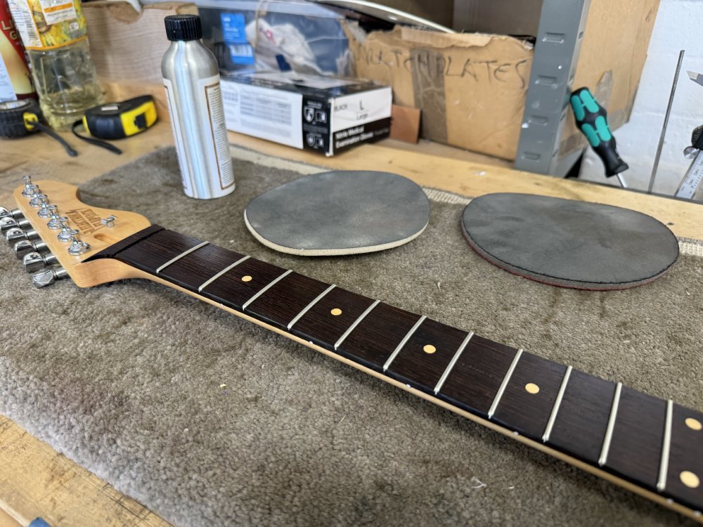 A photo of a guitar neck on a workbench, next to which are some buffing pads and some finishing oil.