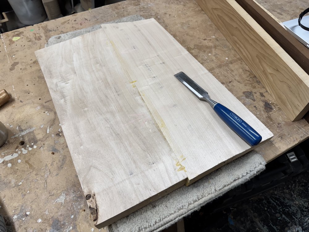 A photo of the two-piece body blank sat on the workbench, showing the excess glue that has built up and solidified on the join line. Atop the body blank sits a large chisel.