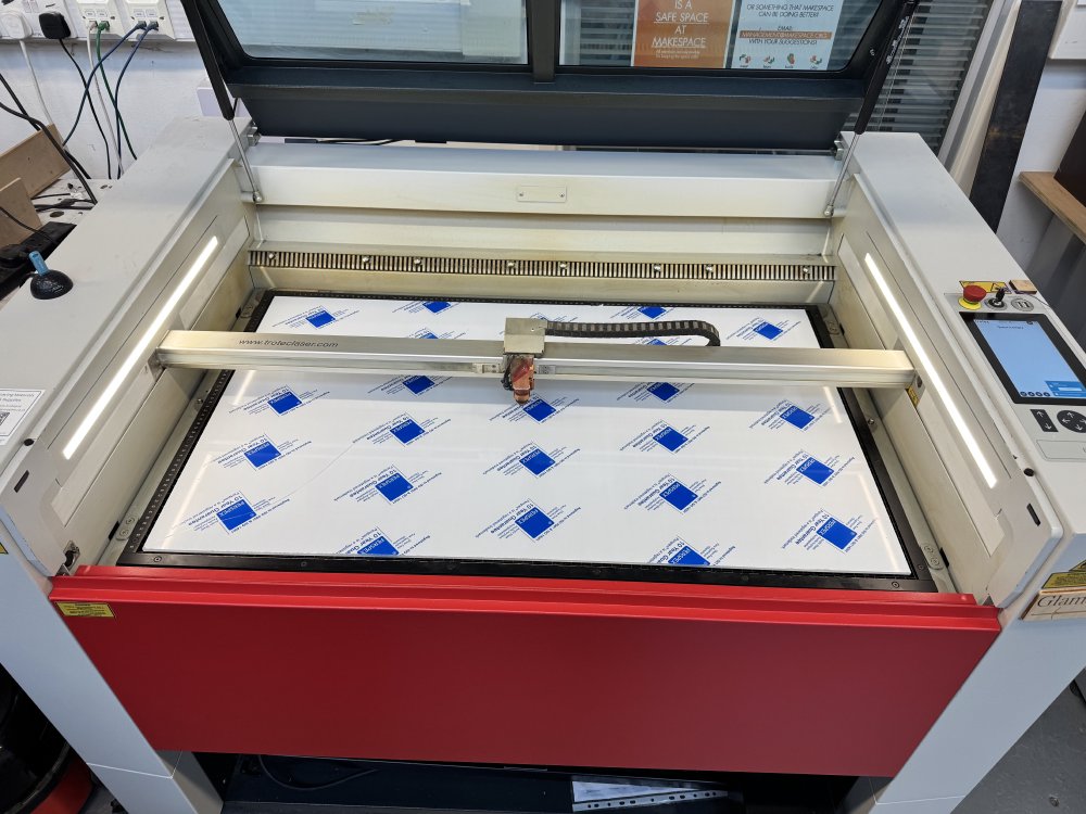 A photo of a table sized laser-cutter. On the bed of the laser-cutter is a large sheet of 5mm thick acrylic, filling the entire bed.