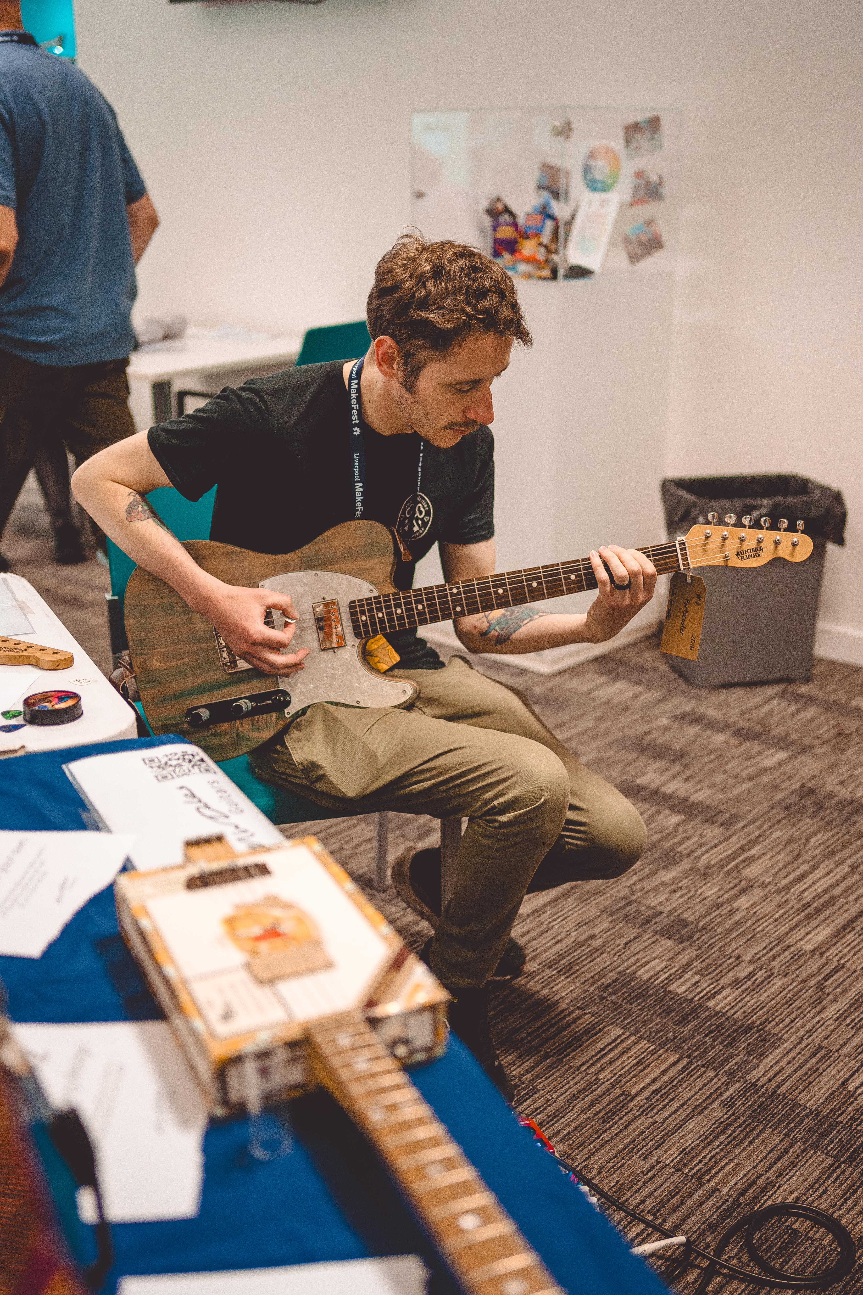 A photo of my brother Tris sat playing the faded blue telecaster style guitar that is the parts build I started with.