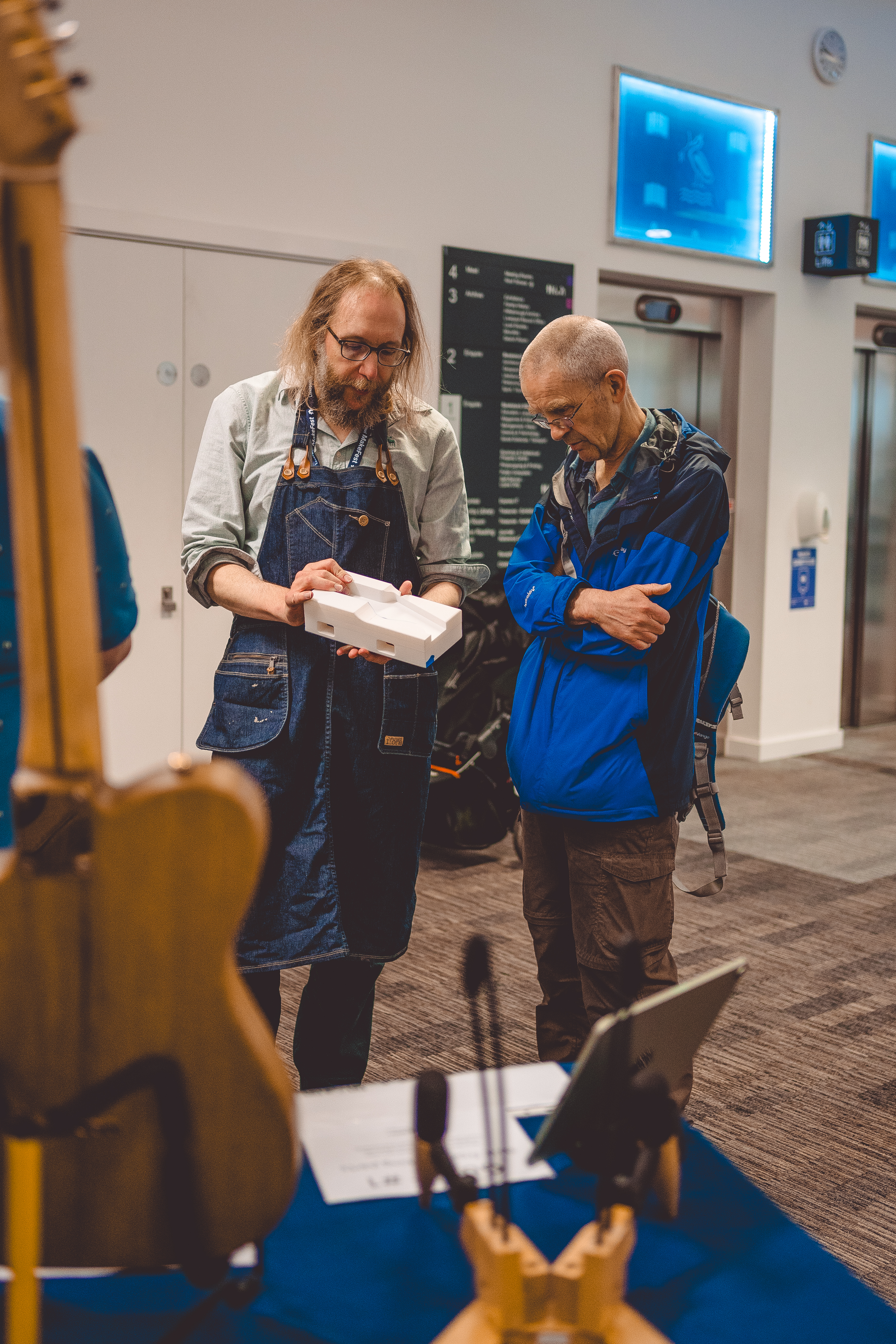 A photo of me talking to another person at Makefest. In my hand I have a large 3D-printed jig that I use to help make guitar necks.