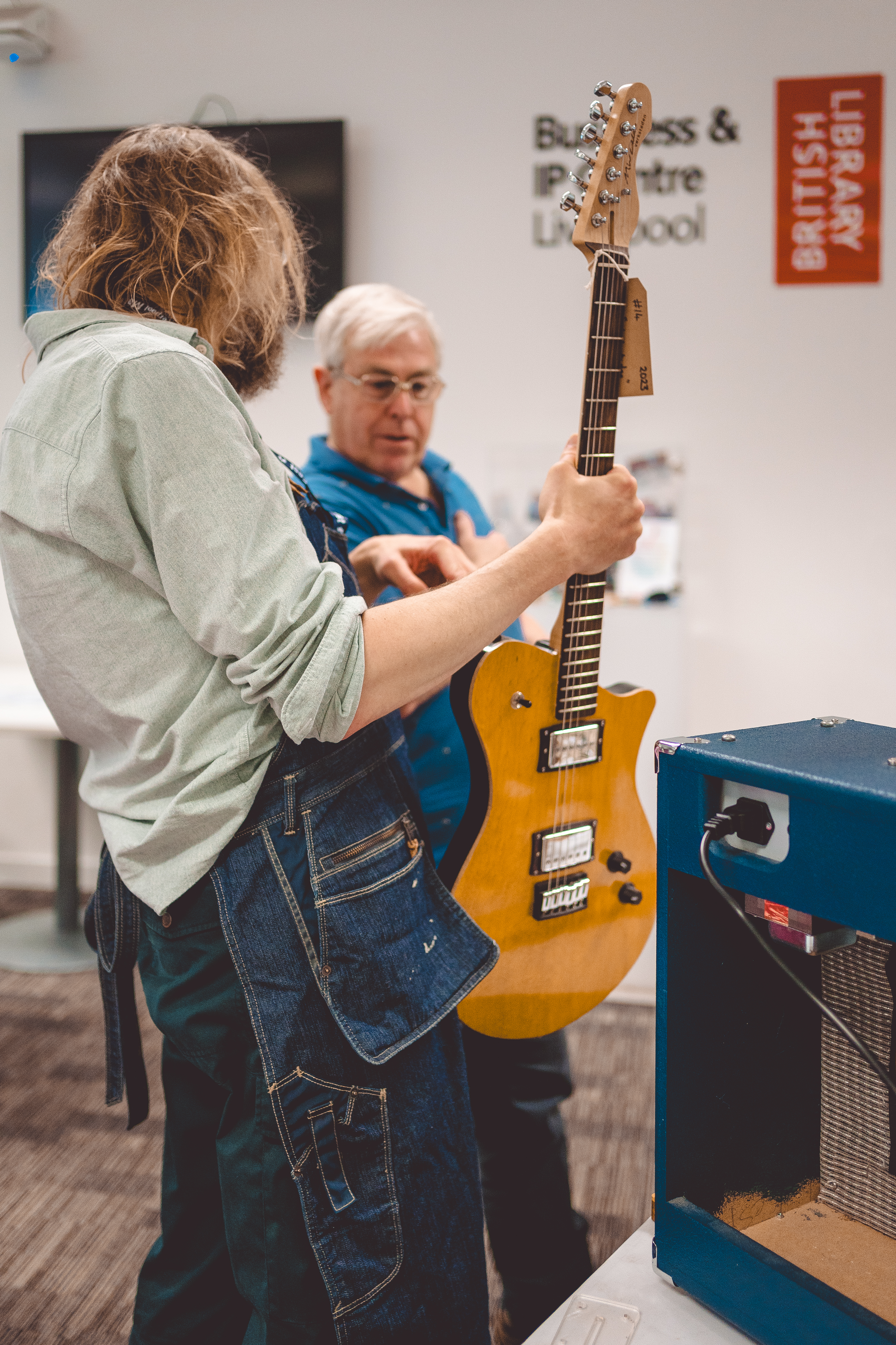 A photo of me holding a guitar showing the back of it to a man who is looking at where I'm pointing. I think I was explaining about how I do the neck joints.