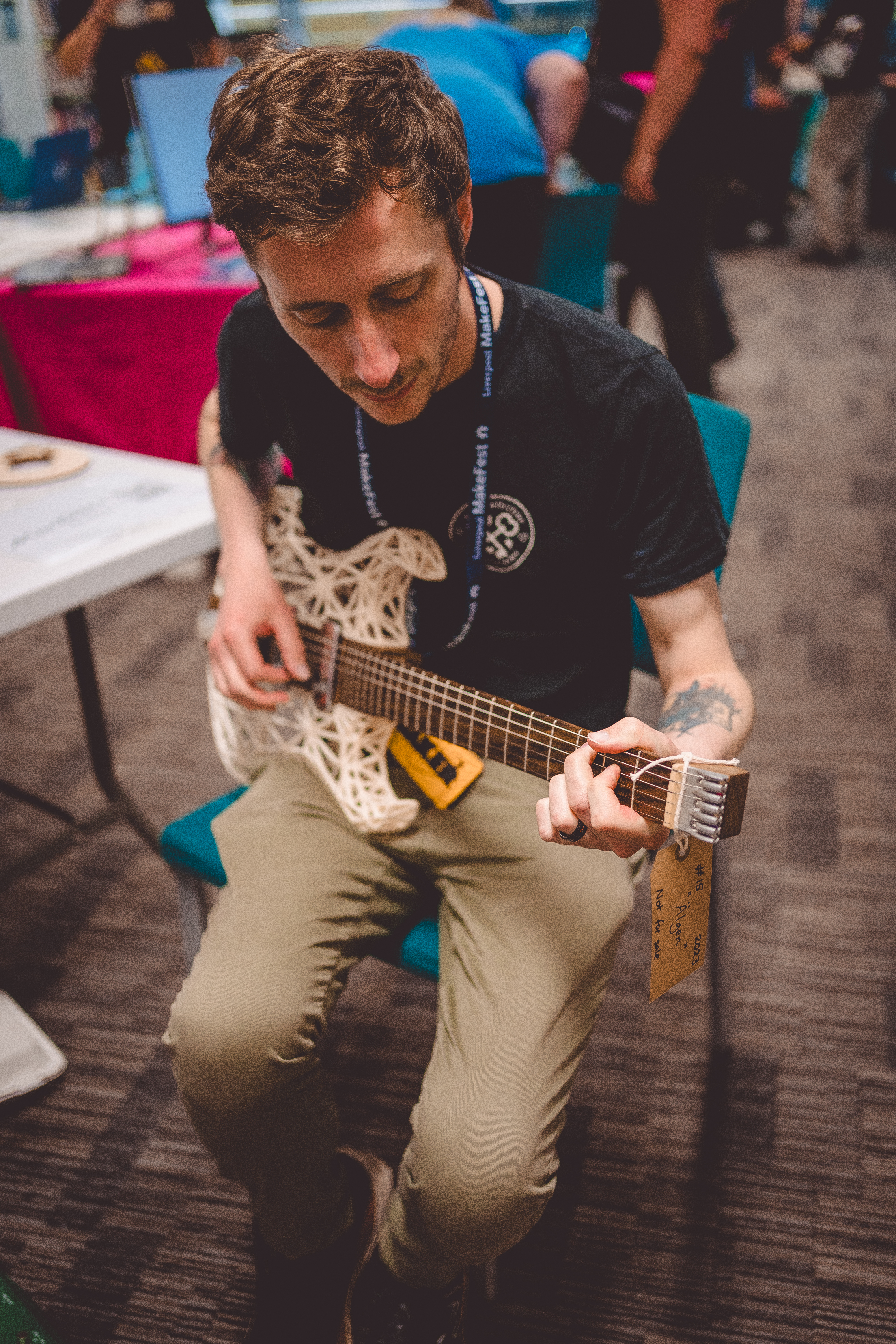 A close up photo of my brother Tris, who is sat playing an unusual looking guitar that is made from a mixture of wood and 3D-printed parts.