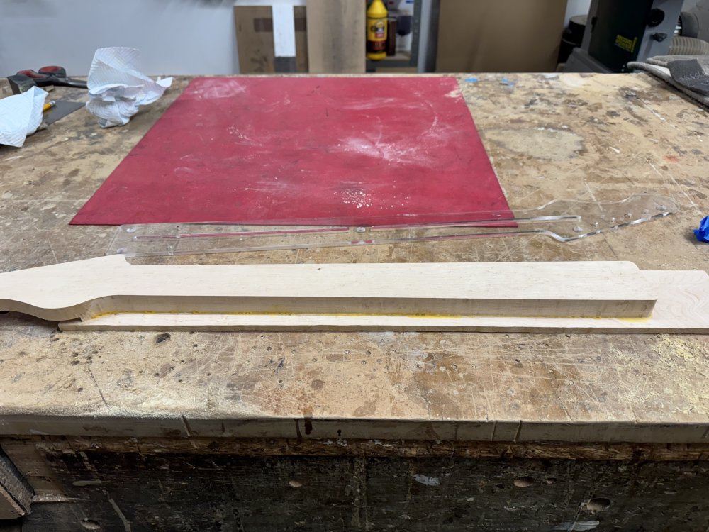 A photo of the main part of a guitar neck (profile cut only, no rear carve yet) glued to the fretboard blank that has yet to be trimmed to match the shape of the rest of the neck. A small amount of glue seapage is visibile along the join line.