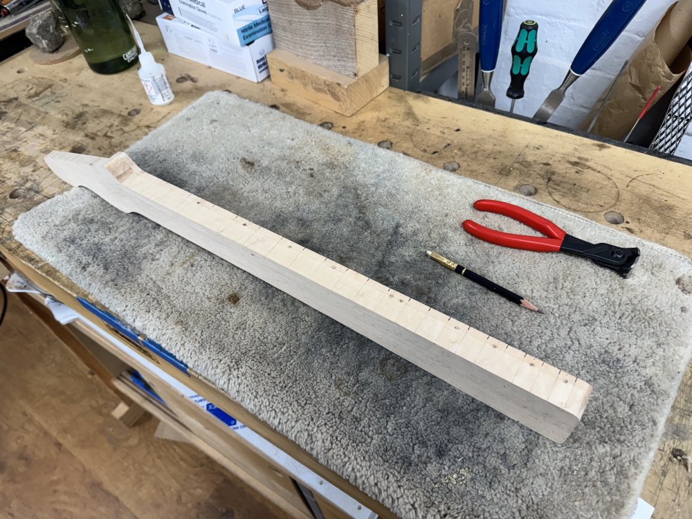 A photo of the neck again, but all the holes for the side inlay markers have been filled with bits of goldish dowel.