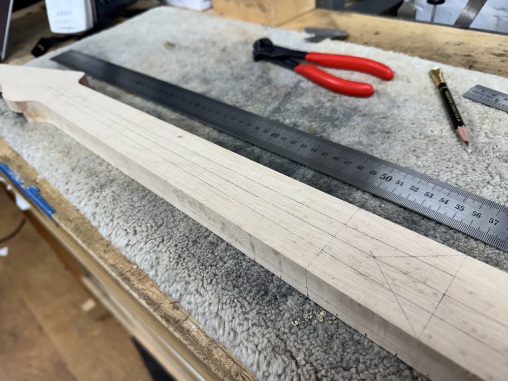A photo of the back of the guitar neck, which hasn't yet been carved. On it is a series of pencil lines that go the length of the neck tapering at a rate different to the taper of the sides of the neck. Next to the neck sit a long ruler and a pencil.
