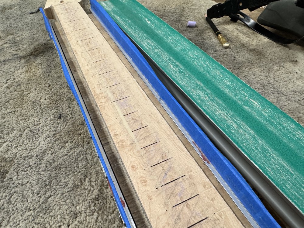A close up photo of the neck in the jig, and you can now see wood-dust on either edge as the concaved beam has been applied to the formerly flat surface. The dust lines however are not perfectly parallel to the direction of the neck as one would ideally want, the have a diagonal slant to them.